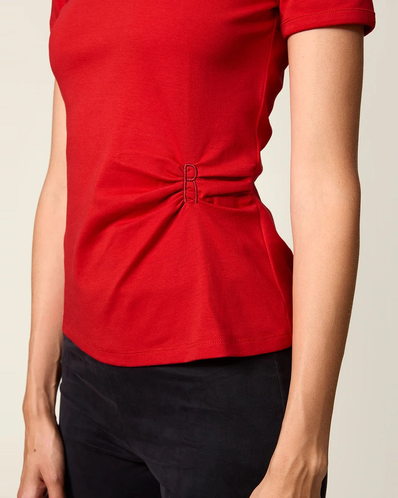 Czerwony, bawełniany t-shirt Nemi Rouje z okrągłym dekoltem i wąskim, krótkim rękawem. Po lewej stronie, w talii posiada ciekawe marszczenie i haftowaną literę R.