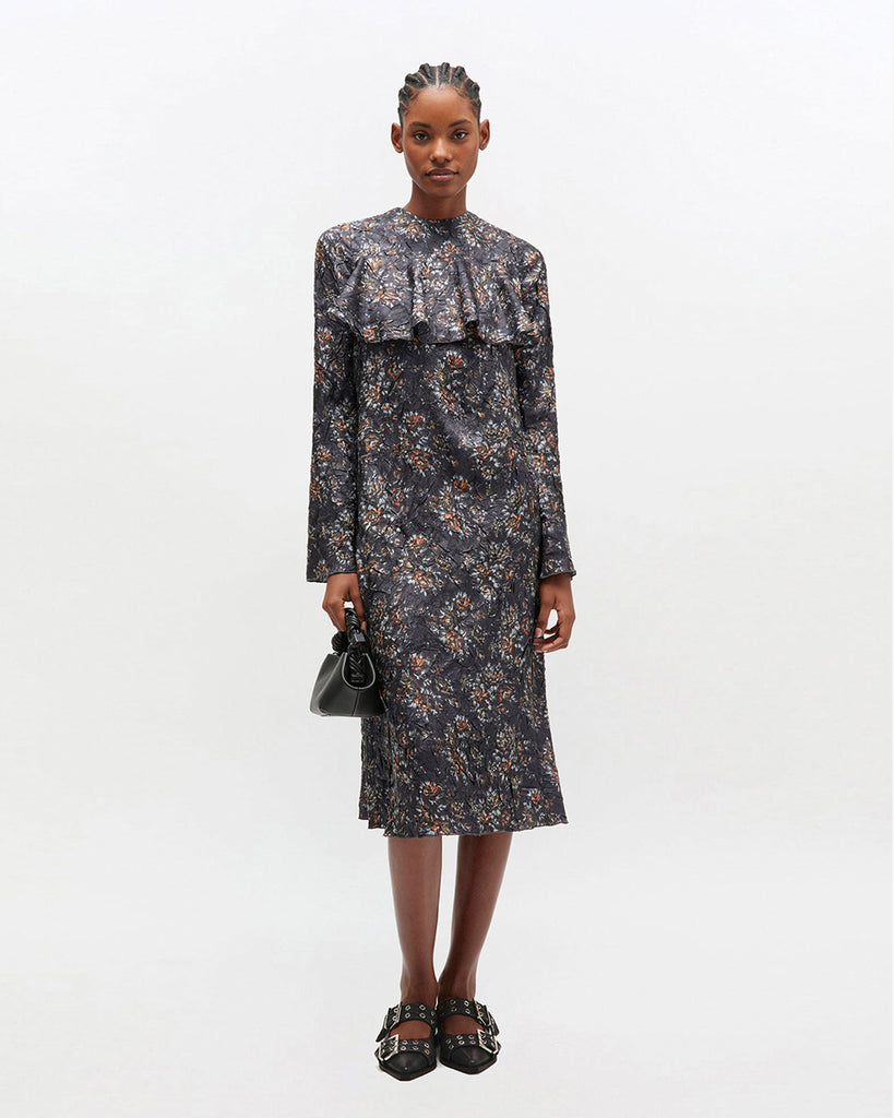 Prosta, midi sukienka 0982 GANNI Shibori Black z okrągłym dekoltem i długimi rękawami. Posiada falbankę na dekolcie i romantyczny, kwiatowy wzór. Wykończona jest plisowanym materiałem shibori. Ma długość za kolano. Idealna na codzień.