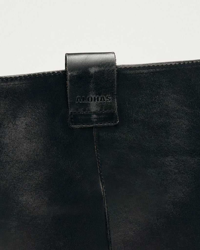 Czarne, masywne kozaki typu oficerki ALOHAS Sajan Black Leather z efektem przetarcia. Wzorowane na tradycyjnych oficerkach z zaokrąglonymi noskami i podwyższoną, gumową podeszwą. Sięgają do łydki. Po bokach posiadają uchwyty z logo marki, które ułatwiają zakładanie. Wykonane z przetarcia czarnej skóry.&nbsp;