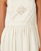 Biała, letnia sukienka midi na cienkich ramiączkach Riverini Sessun z prostym dekoltem i z odkrytymi plecami z wiązaniem na krzyż. Z przodu posiada piękny, ażurowy haft. Wcięta w talii i rozkloszowana u dołu.