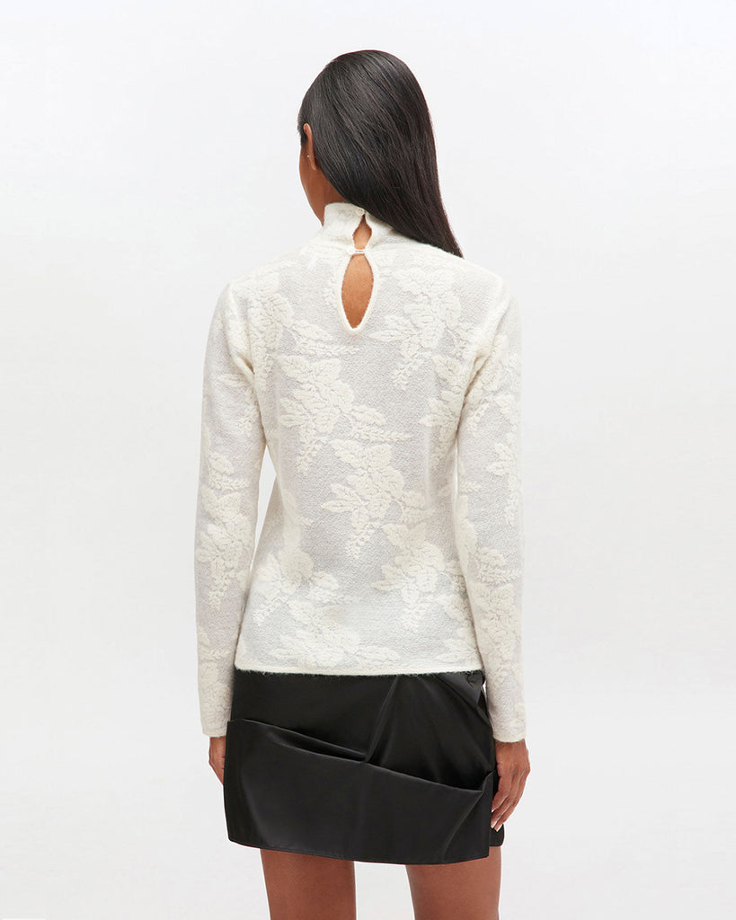 Lekko prześwitujący golf 2643 GANNI Egret z wysokim kołnierzykiem i długimi rękawami z kwiatowym printem. Posiada zapięcie na ozdobne guziczki z tyłu. Idealny do spódnicy lub luźnych spodni. Wykonany z tkaniny z alpaką i wełną.
