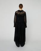 Długa, przezroczysta sukienka Sheer Lace Maxi z koronki z cekinami. Ma zabudowany, efektowny dekolt oraz długie rękawy. Z przodu, na długości ma zapięcia. Można ją nosić zapięta jako sukienkę, bądź rozpiętą jako pelerynę. Sukienka nie posiada podszewki.&nbsp;