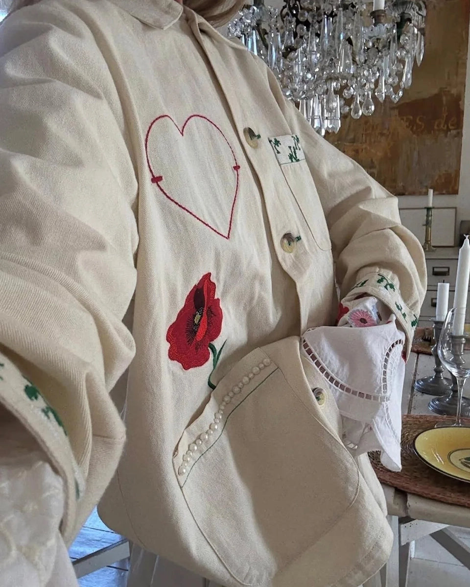 Cienka, luźna, koszulowa kurtka Bea SISSEL EDELBO z kołnierzykiem i długimi rękawami zakończonymi mankietami. Zapinana na duże guziki. Kurtka posiada trzy, duże, prostokątne kieszenie z przodu. Dolne kieszenie obszyte zostały drobnymi perełkami. Kurtka dekorowana jest efektownymi haftami z motywami kwiatów, serca i biedronki