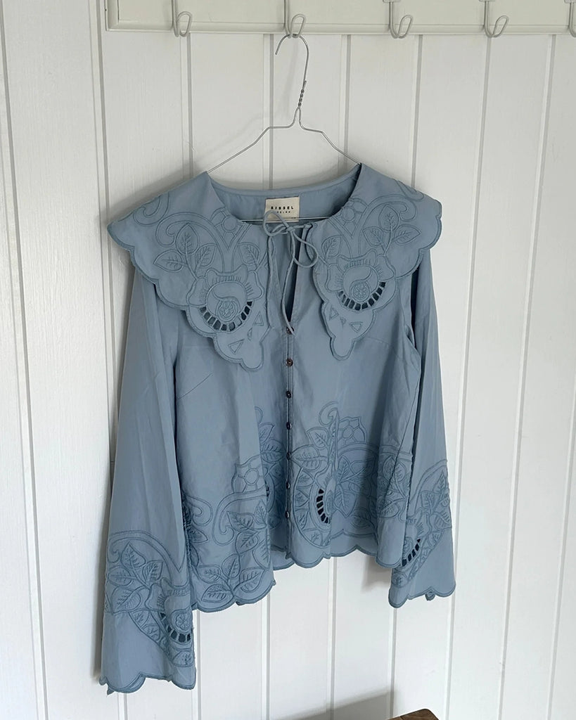 Romantyczna, koszulowa bluzka Cameron SISSEL EDELBO z dużym, efektownym kołnierzem i długim, rozszerzanym rękawem. Wiązana pod szyją. Zapinana na guziki z masy perłowej i haftki