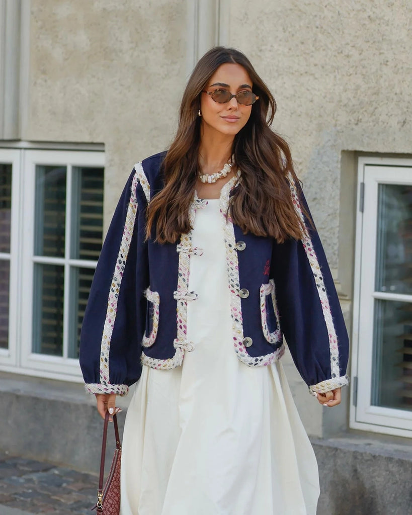 Cienka, krótka kurtka Como SISSEL EDELBO o pudełkowym kroju z długimi, balonowymi rękawami. Zapinana na duże guziki i haftki. Wykończona zaokrąglonymi rogami i grubą lamówką z tkaniny boucle