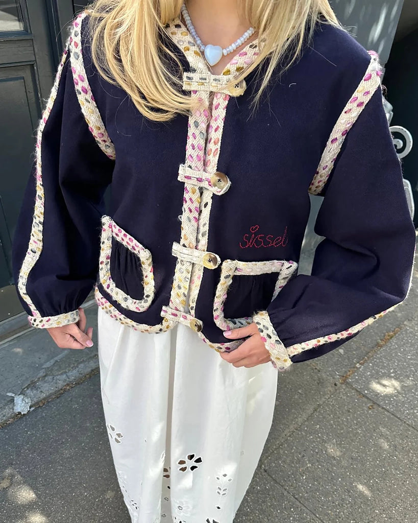 Cienka, krótka kurtka Como SISSEL EDELBO o pudełkowym kroju z długimi, balonowymi rękawami. Zapinana na duże guziki i haftki. Wykończona zaokrąglonymi rogami i grubą lamówką z tkaniny boucle