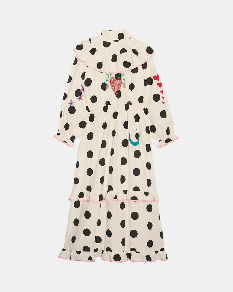 Bawełniana sukienka maxi w grochy Diana SISSEL EDELBO z długimi, balonowymi rękawami, wysokim kołnierzykiem i efektowną falbaną przy dekolcie. Zwężana i elastyczna w talii. U dołu i przy mankietach wykończona falbankami. Dekorowana uroczymi, kolorowymi haftami z motywami serc, kwiatów, gwiazd i księżyca. Obszyta różową lamówką. Sukienka ma długość do kostek