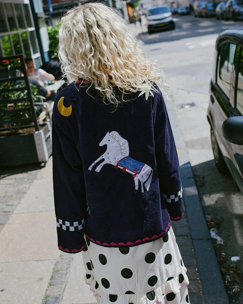 Cienka, krótka, sztruksowa kurtka Maggie SISSEL EDELBO z okrągłym dekoltem i szerokimi rękawami. Dekorowana pięknymi, ręcznie wykonanymi haftami z motywami geometrycznymi, solarnymi i cyrkowymi. Zapinana na guziki. Z przodu posiada dwie, duże kieszenie.