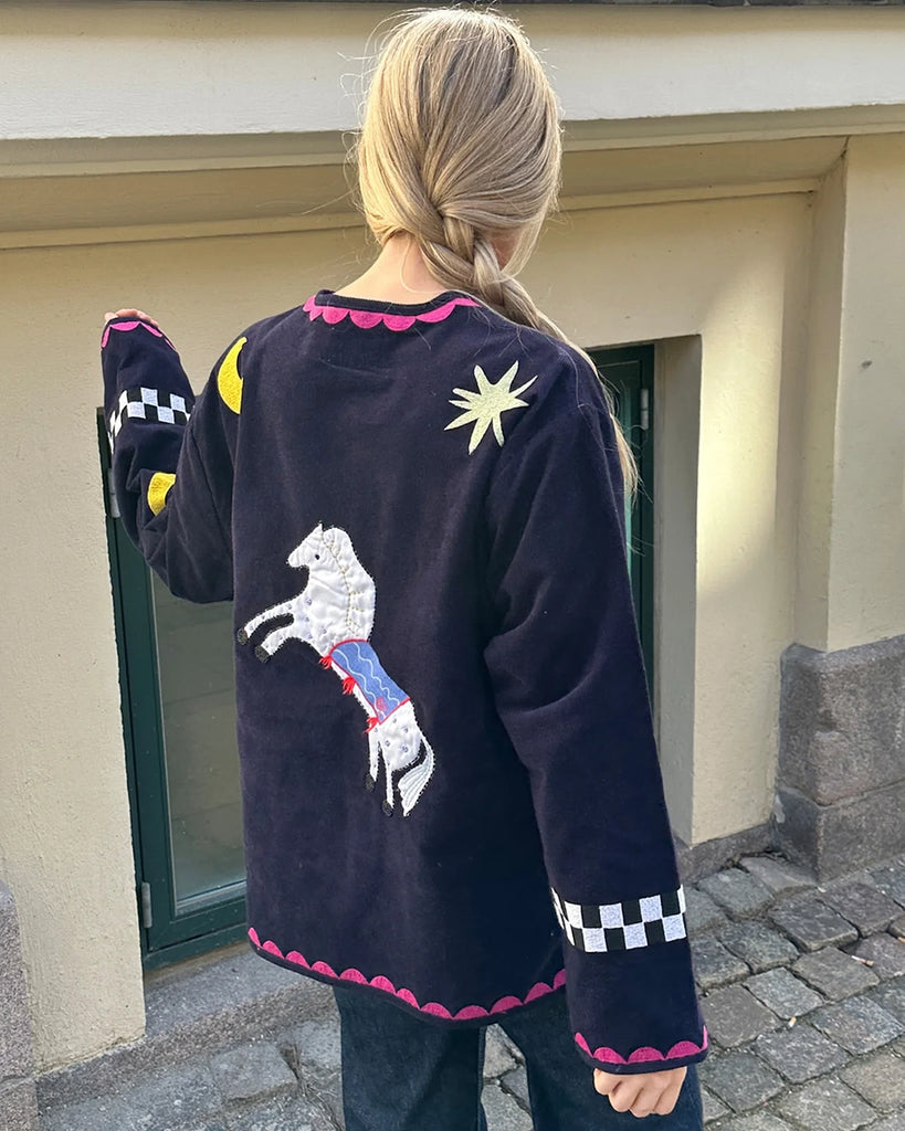 Cienka, krótka, sztruksowa kurtka Maggie SISSEL EDELBO z okrągłym dekoltem i szerokimi rękawami. Dekorowana pięknymi, ręcznie wykonanymi haftami z motywami geometrycznymi, solarnymi i cyrkowymi. Zapinana na guziki. Z przodu posiada dwie, duże kieszenie.