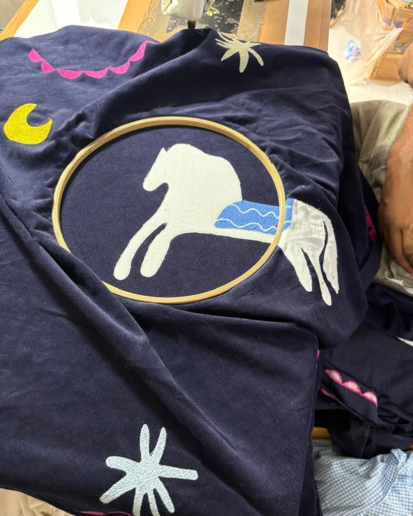 Cienka, krótka, sztruksowa kurtka Maggie SISSEL EDELBO z okrągłym dekoltem i szerokimi rękawami. Dekorowana pięknymi, ręcznie wykonanymi haftami z motywami geometrycznymi, solarnymi i cyrkowymi. Zapinana na guziki. Z przodu posiada dwie, duże kieszenie.