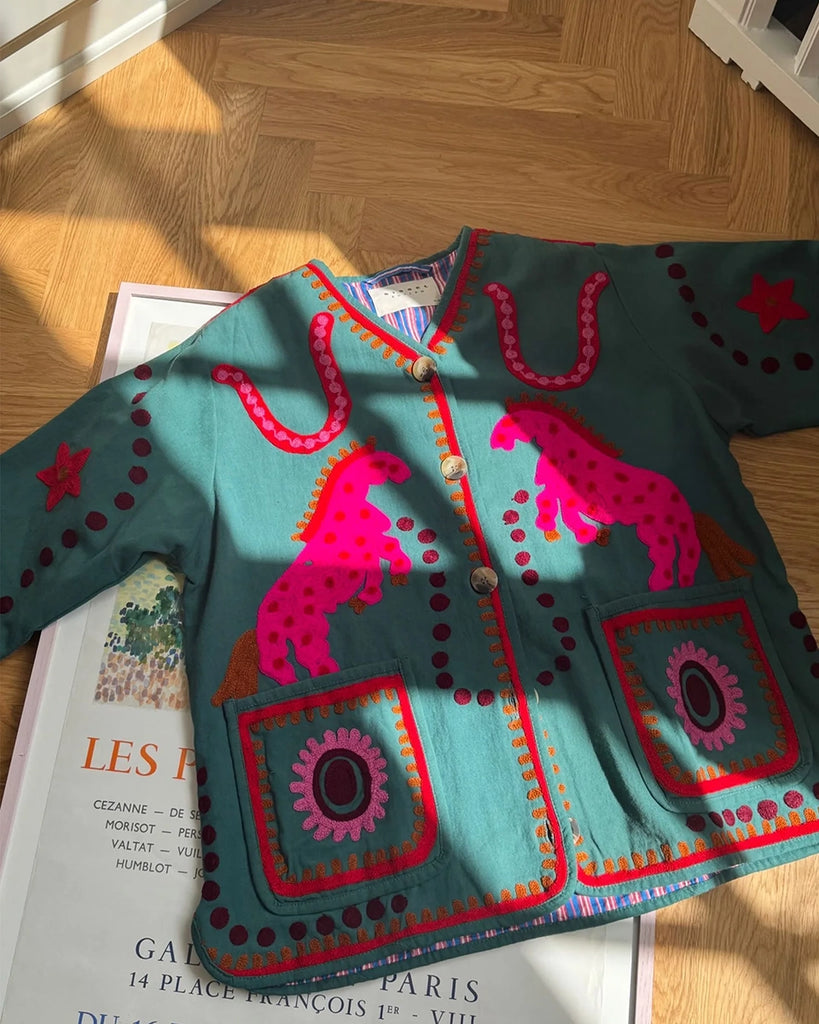 Cienka, krótka kurtka Maggie SISSEL EDELBO z trójkątnym dekoltem i szerokimi rękawami. Dekorowana pięknymi, ręcznie wykonanymi haftami suzani w soczystych, neonowych odcieniach różu . Zapinana na guziki. Z przodu posiada dwie, duże kieszenie.