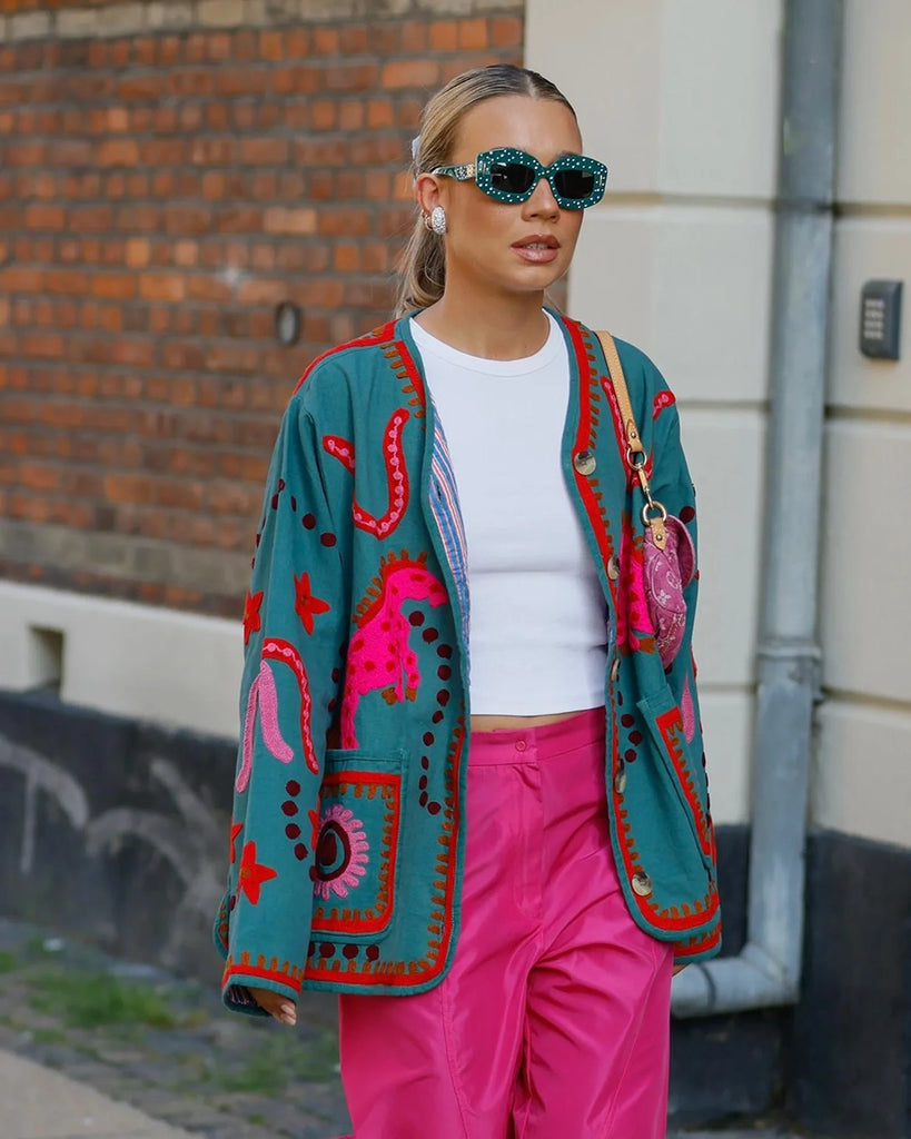 Cienka, krótka kurtka Maggie SISSEL EDELBO z trójkątnym dekoltem i szerokimi rękawami. Dekorowana pięknymi, ręcznie wykonanymi haftami suzani w soczystych, neonowych odcieniach różu . Zapinana na guziki. Z przodu posiada dwie, duże kieszenie.