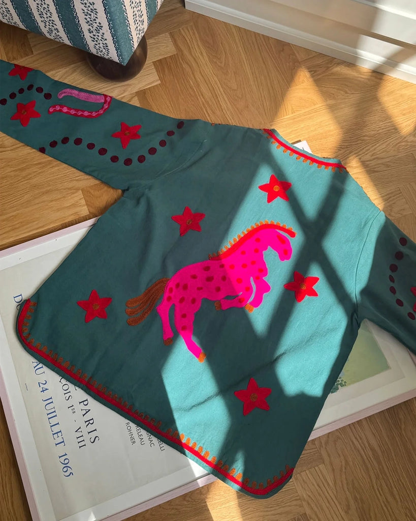 Cienka, krótka kurtka Maggie SISSEL EDELBO z trójkątnym dekoltem i szerokimi rękawami. Dekorowana pięknymi, ręcznie wykonanymi haftami suzani w soczystych, neonowych odcieniach różu . Zapinana na guziki. Z przodu posiada dwie, duże kieszenie.