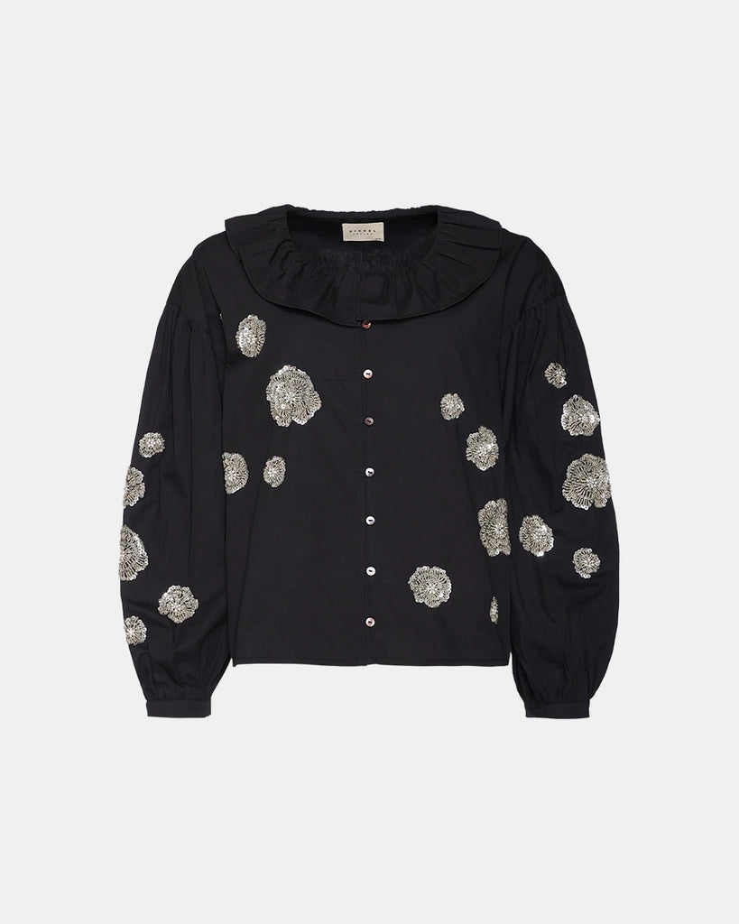 Luźna, bawełniana bluzka Mildred SISSEL EDELBO z okrągłym dekoltem obszytym falbanką, opadającymi ramionami i szerokimi, balonowymi, długimi rękawami. Zapinana na drobne guziki z masy perłowej i elastyczne. Dekorowana efektownymi, kwiatowymi aplikacjami ze srebrnych cekinów i koralików.