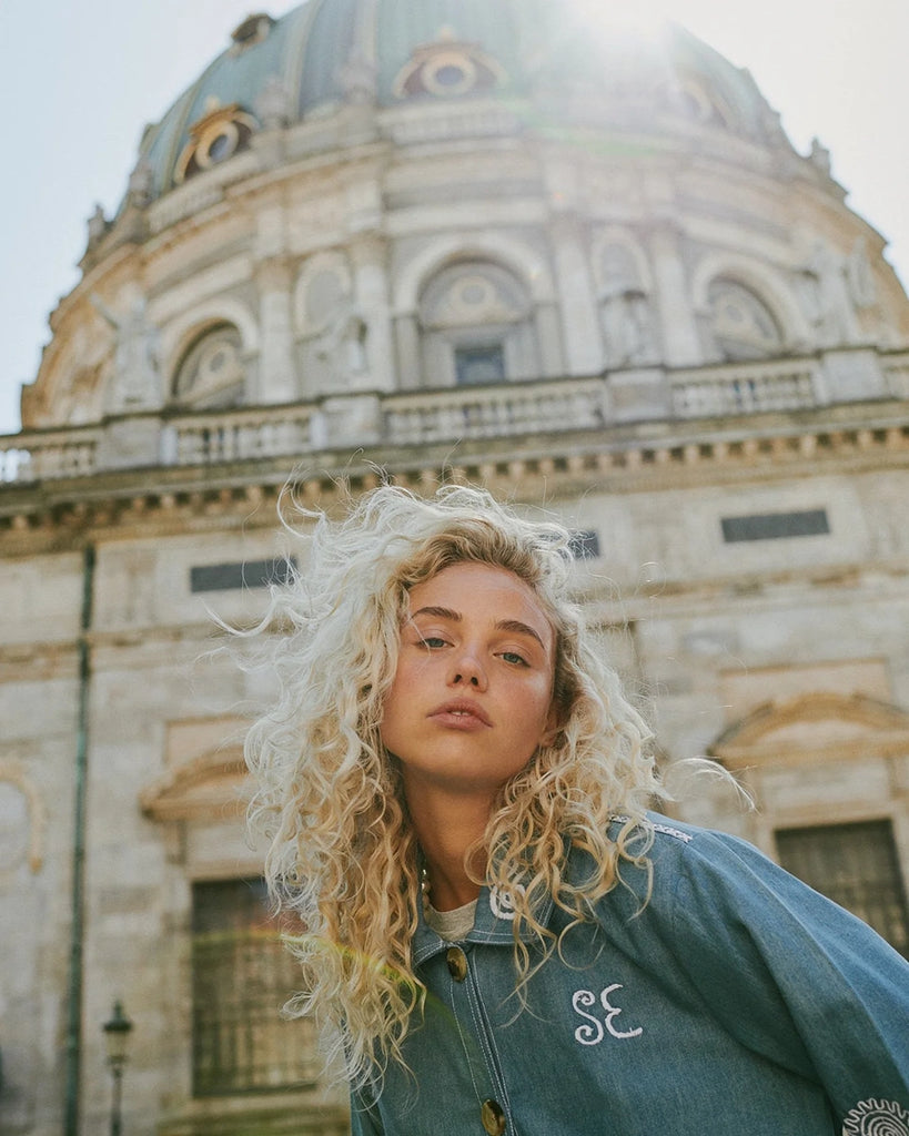 Cienka, oversizowa kurtka jeansowa My SISSEL EDELBO o koszulowym kroju. Posiada kołnierzyk i długie, luźne rękawy. Wykonana ze sztywnego denimu z końcówek produkcyjnych. Dekorowana pięknymi, białymi haftami. Zapinana na duże guziki. Posiada dwie, przednie kieszenie.