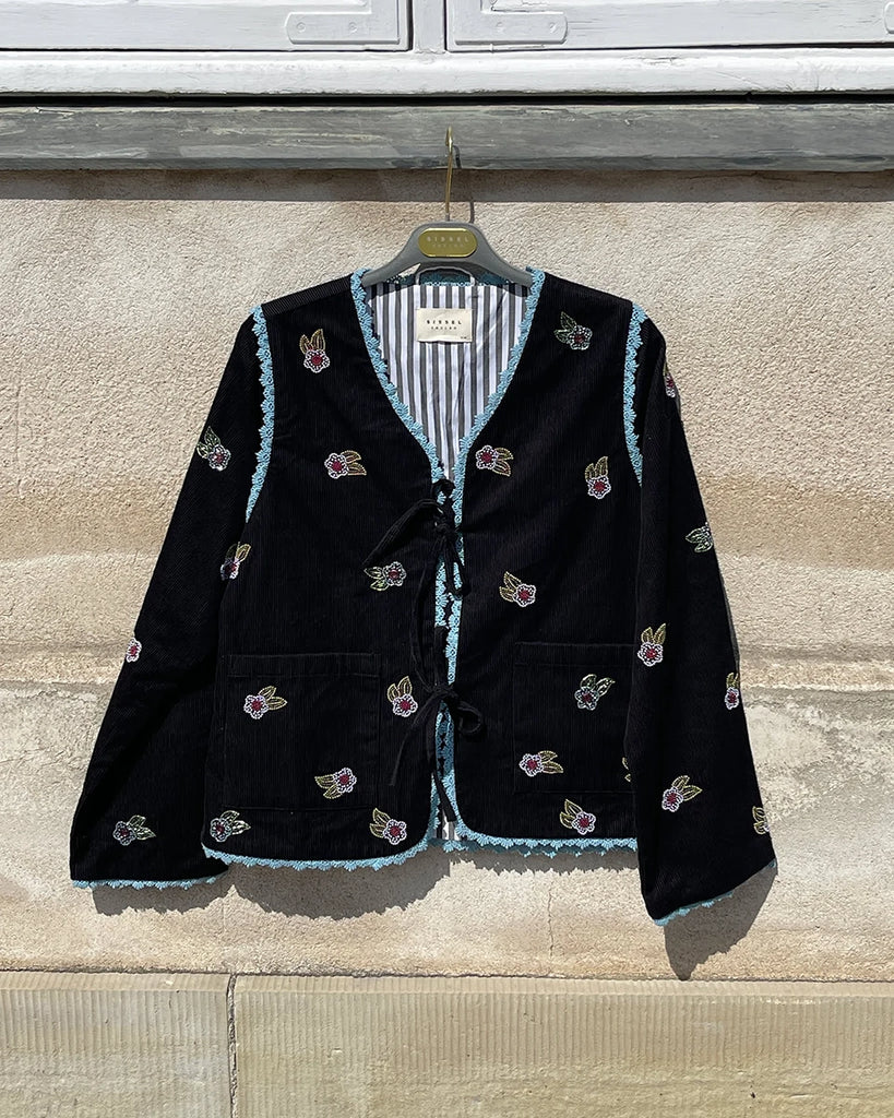 Cienka, krótka, sztruksowa kurtka Tahlia SISSEL EDELBO z trójkątnym dekoltem, wiązana z przodu na kokardki. Wyszywana kolorowymi, drobnymi koralikami w uroczy, kwiatowy wzór. Wykończona drobną, kontrastową koronką.