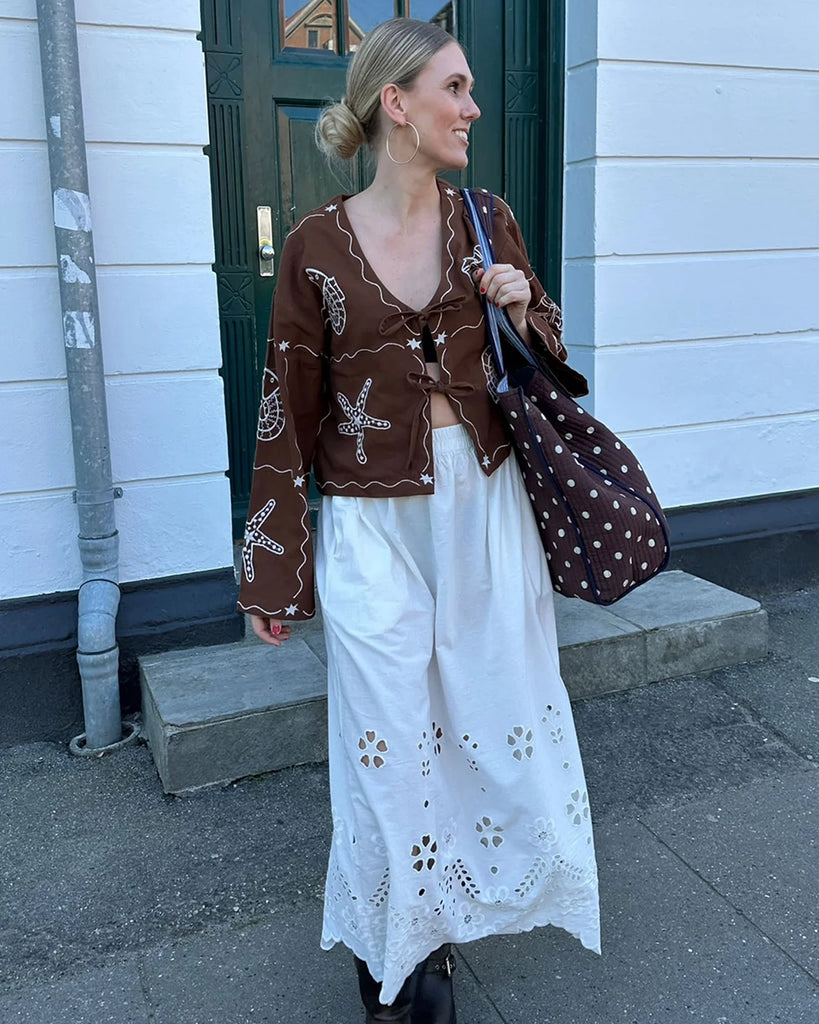 Luźna bluzka Seashell SISSEL EDELBO z długim, szerokim rękawem i głębokim dekoltem w serek. Z przodu wiązana na kokardki. Wyszywana ręcznie w piękne, morskie motywy muszli, ryb i rozgwiazd. 