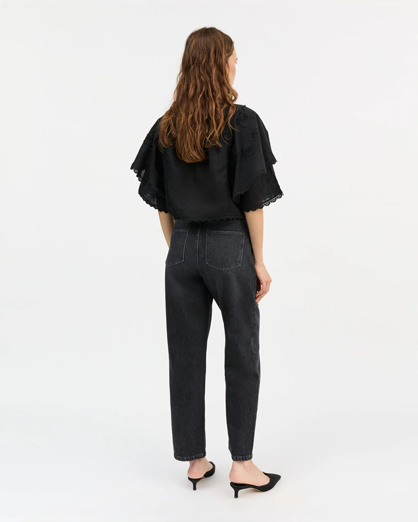 Lniana bluzka Jardin Black marki SKALL w kolorze czarnym o skróconej długości i z okrągłym dekoltem. Ma szerokie, warstwowe, krótkie rękawy zakończone koronkową lamówką, które tworzą efekt lekkich falban. Z przodu, na środku znajduje się bogaty haft w kwiatowe i ornamentalne wzory.