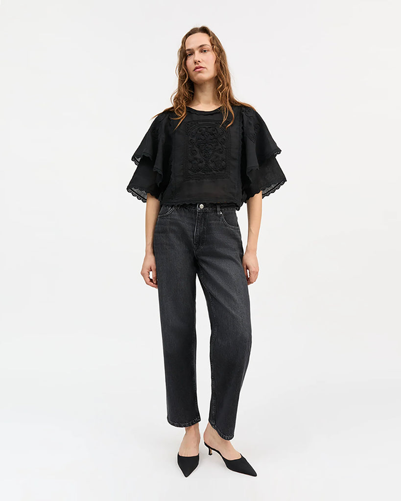 Lniana bluzka Jardin Black marki SKALL w kolorze czarnym o skróconej długości i z okrągłym dekoltem. Ma szerokie, warstwowe, krótkie rękawy zakończone koronkową lamówką, które tworzą efekt lekkich falban. Z przodu, na środku znajduje się bogaty haft w kwiatowe i ornamentalne wzory.