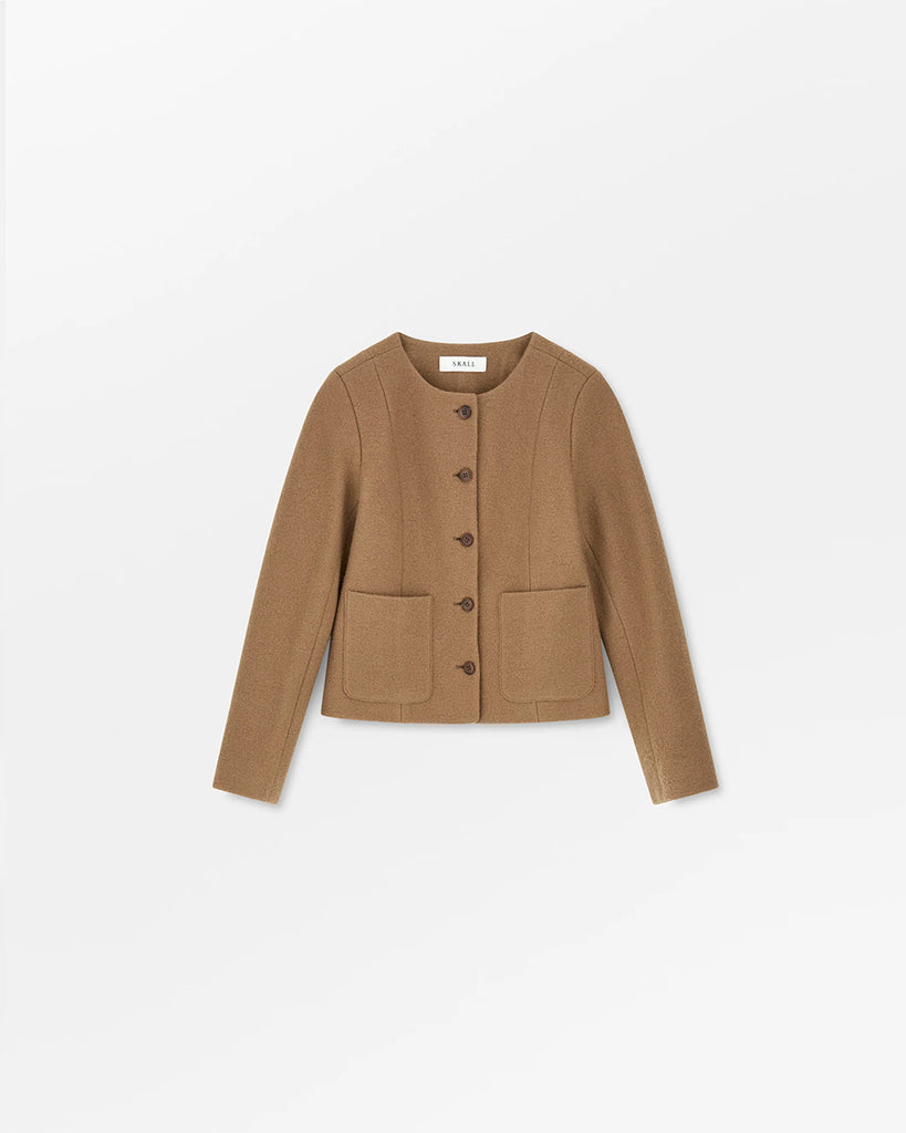 Prosta, lekko pudełkowa kurtka Mona marki SKALL w kolorze karmelowym, z okrągłym dekoltem bez kołnierza, uszyta ze 100% wełny i zapinana z przodu na pięć guzików. Rękawy są długie i proste. Posiada dwie duże kieszenie naszywane z przodu. Podszewka wykonana jest z bawełny organicznej.