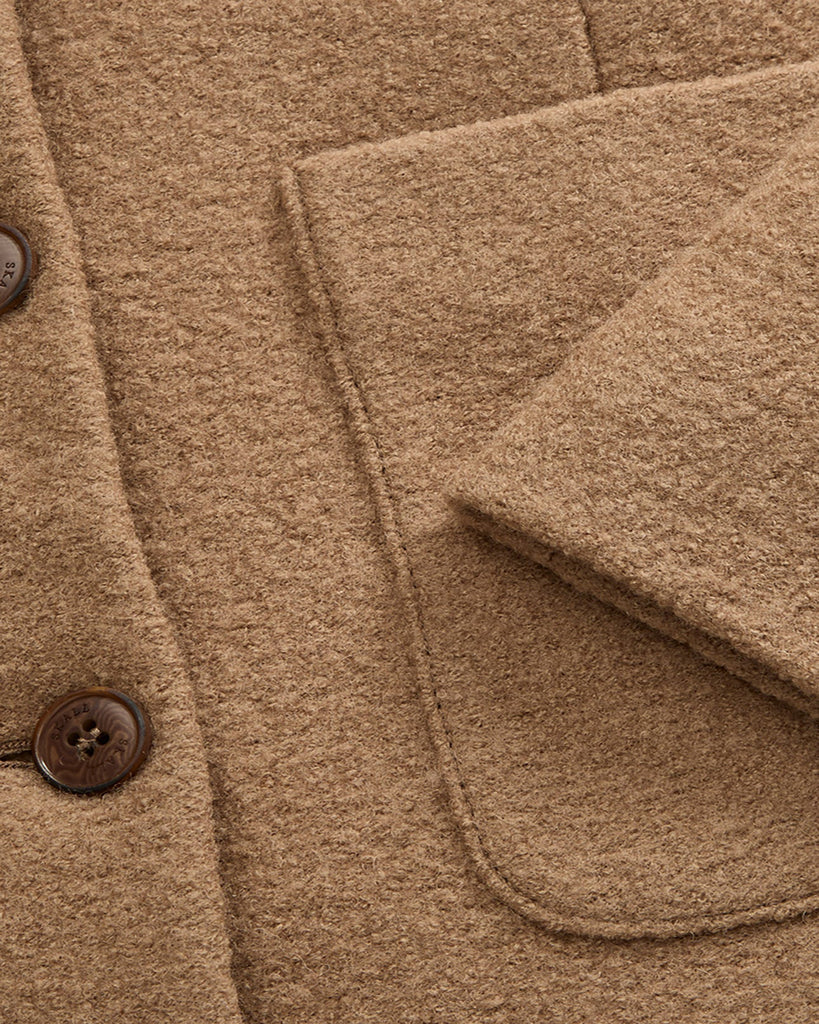 Prosta, lekko pudełkowa kurtka Mona marki SKALL w kolorze karmelowym, z okrągłym dekoltem bez kołnierza, uszyta ze 100% wełny i zapinana z przodu na pięć guzików. Rękawy są długie i proste. Posiada dwie duże kieszenie naszywane z przodu. Podszewka wykonana jest z bawełny organicznej.