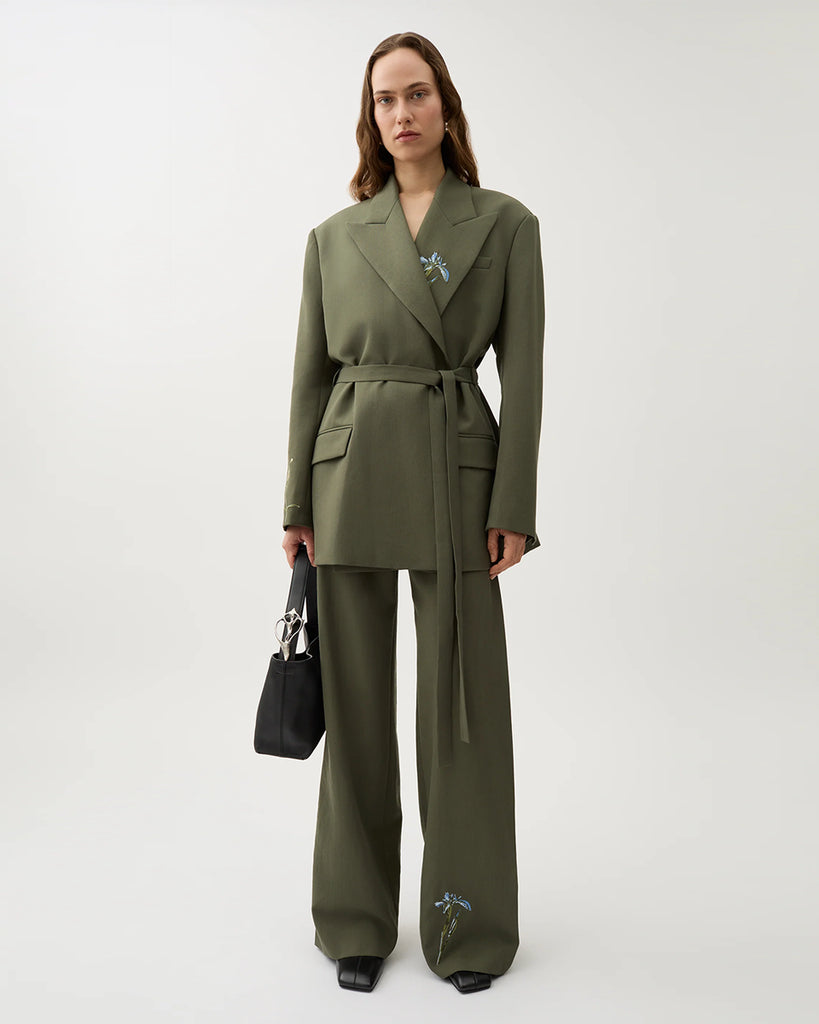 Oversizowa marynarka Stand Dark Moss w kolorze oliwkowej zieleni o wyrazistym, nowoczesnym kroju z haftowanymi zdobieniami w postaci kwiatów. Posiada szerokie klapy w stylu garniturowym oraz pasek w talii, który dodaje kobiecego charakteru. Ma asymetryczne zapięcie, bez widocznych guzików z przodu oraz klasyczne kieszenie z klapką. Zestaw ze spodniami Nora Dark Moss lub z ulubionymi jeansami.