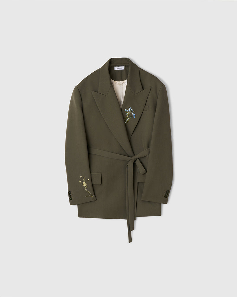 Oversizowa marynarka Stand Dark Moss w kolorze oliwkowej zieleni o wyrazistym, nowoczesnym kroju z haftowanymi zdobieniami w postaci kwiatów. Posiada szerokie klapy w stylu garniturowym oraz pasek w talii, który dodaje kobiecego charakteru. Ma asymetryczne zapięcie, bez widocznych guzików z przodu oraz klasyczne kieszenie z klapką. Zestaw ze spodniami Nora Dark Moss lub z ulubionymi jeansami.