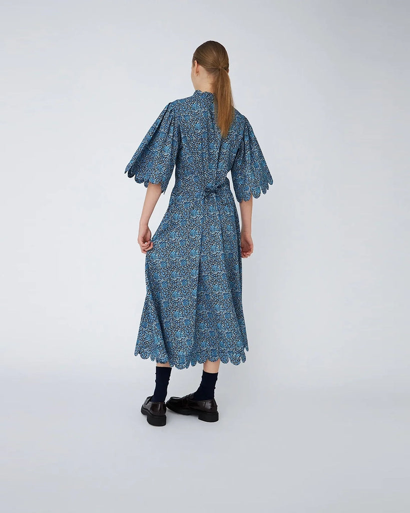 Luźna, bawełniana sukienka midi w kwiatowy print STELLA NOVA z wysokim dekoltem w formie stójki i szerokim, krótkim rękawem o długości do łokcia. W górnej partii zapinana na guziki. Z tyłu wiązana w talii. Wykończona muszelkowo. Sukienka ma długość do połowy łydki.