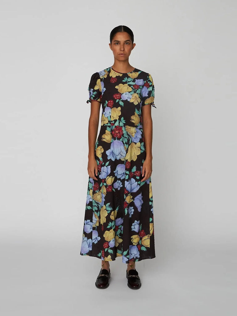 Zwiewna sukienka maxi Flowered Cotton STELLA NOVA w efektowny, kolorowy, kwiatowy print. Posiada okrągły dekolt i krótki, wiązany po bokach rękaw. Jest lekko zwężana w talii i rozkloszowana u dołu. 
