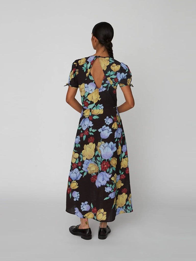 Zwiewna sukienka maxi Flowered Cotton STELLA NOVA w efektowny, kolorowy, kwiatowy print. Posiada okrągły dekolt i krótki, wiązany po bokach rękaw. Jest lekko zwężana w talii i rozkloszowana u dołu. 