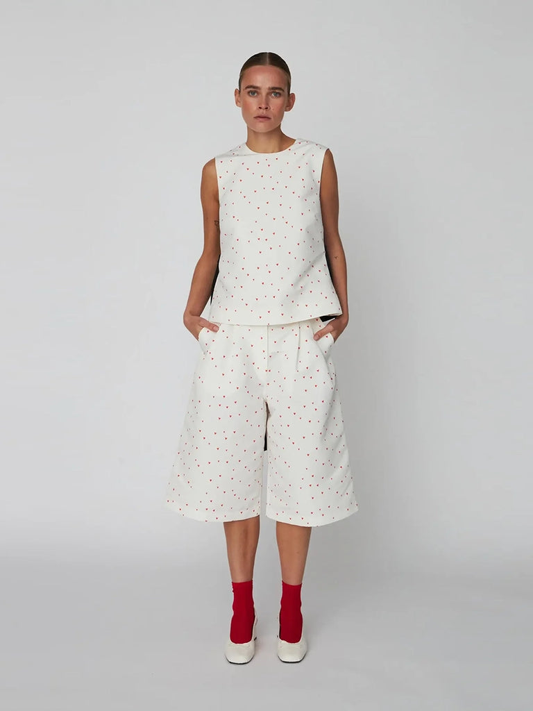 Luźny top bez rękawów Heart Printed Bow STELLA NOVA w uroczy print w serduszka. Lekko rozkloszowana u dołu. Posiada okrągły dekolt. Na plecach ma głębokie wycięcie w kształcie litery V oraz dużą, efektowną, czarną kokardę