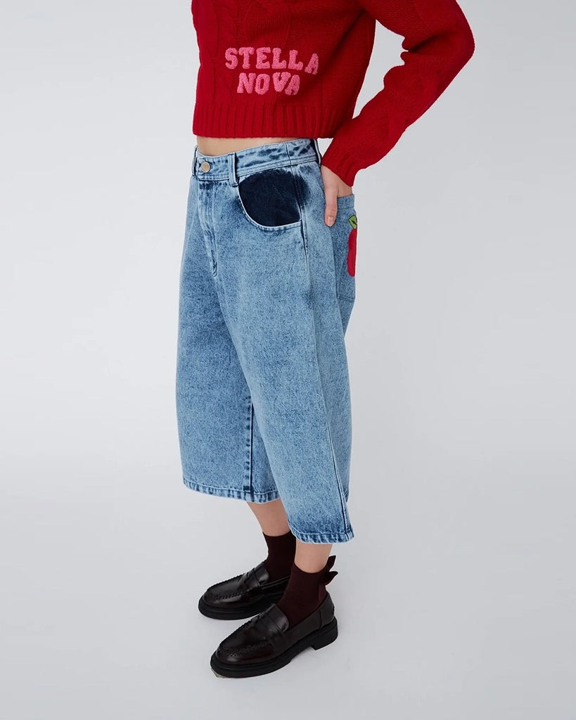 Luźne, jeansowe szorty STELLA NOVA z niskim stanem i szeroką nogawką o długości za kolana. Wykonane z jeansu z efektem "sprania". Szorty mają dwie, przednie kieszenie ufarbowane na ciemnogranatowy kolor. Na lewej, tylnej kieszeni spodnie posiadają naszywkę z uroczym motywem jabłka.