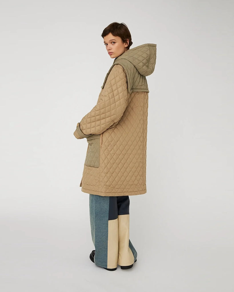 Długa, overisozwa, pikowana kurtka STELLA NOVA z kapturem i szerokimi rękawami. Posiada kontrastowe elementy. Z przodu zapinana na duże haftki i guziki imitujące poroże. Kurtka ma dwie, przednie kieszenie. Posiada długość do kolan.