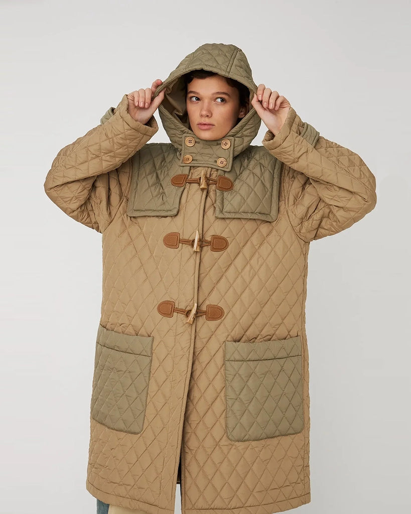 Długa, overisozwa, pikowana kurtka STELLA NOVA z kapturem i szerokimi rękawami. Posiada kontrastowe elementy. Z przodu zapinana na duże haftki i guziki imitujące poroże. Kurtka ma dwie, przednie kieszenie. Posiada długość do kolan.