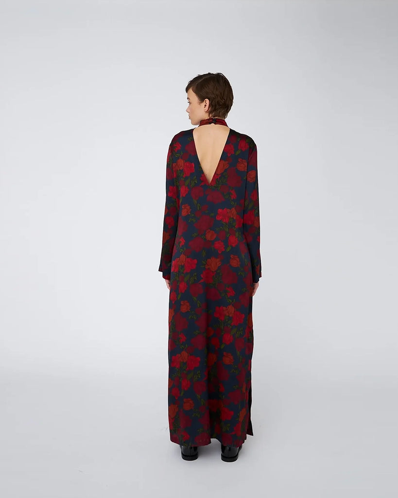 Jedwabna, elegancka sukienka maxi w kwiatowy wzór STELLA NOVA z długim rękawem i dekoltem w formie krótkiego golfu zapinanego z tyłu na szyi za pomocą guzikow. Na plecach posiada głębokie, trójkątne wycięcie. Sukienka ma rozcięcie u dołu