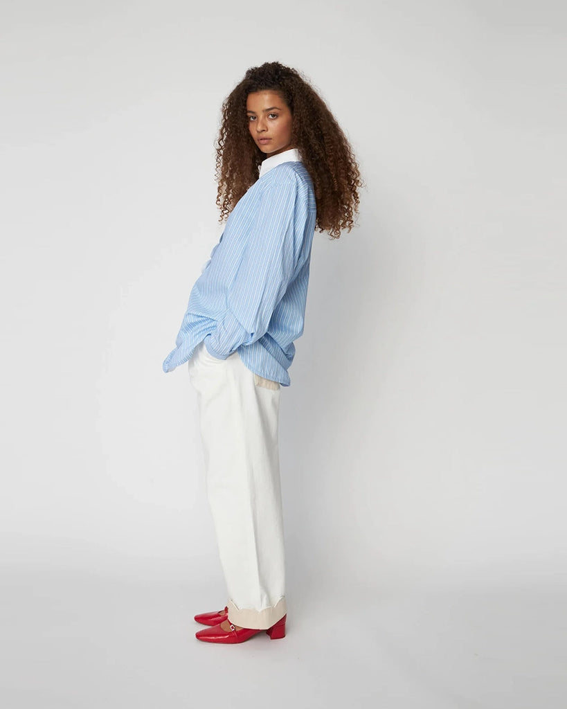 Oversizowa, niebieska koszula w cienkie paski Striped Shirt STELLA NOVA z kontrastowym kołnierzykiem i muszelkowym wykończeniem przy dekolcie. U góry zapinana na guziki.