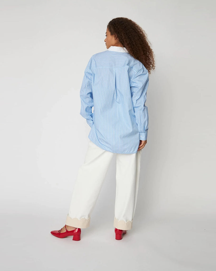 Oversizowa, niebieska koszula w cienkie paski Striped Shirt STELLA NOVA z kontrastowym kołnierzykiem i muszelkowym wykończeniem przy dekolcie. U góry zapinana na guziki.