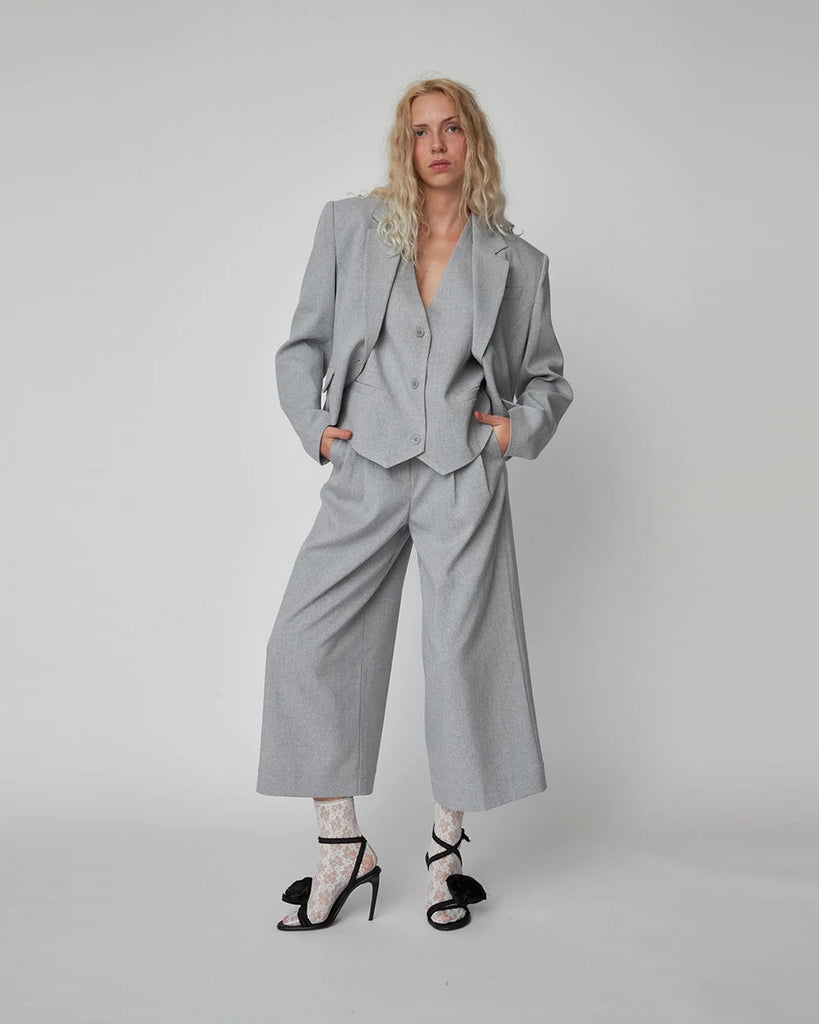 Luźna, szara, garniturowa kamizelka Suiting Vest STELLA NOVA z dekoltem w serek. Z tyłu wykonana z kontrastowej tkaniny. Na plecach u dołu zapinana i zwężana za pomocą regulowanego paska.