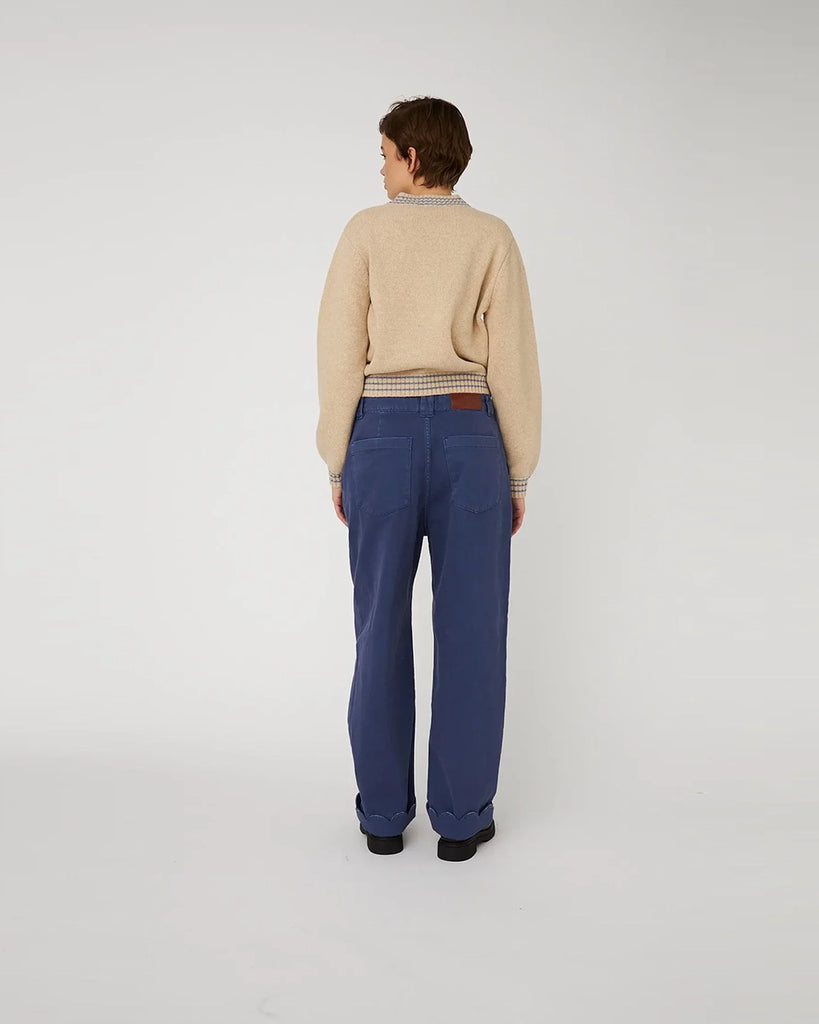 Krótki, beżowy sweter STELLA NOVA z dużym, haftowanym jabłkiem nad lewą piersią. Sweter ma okrągły dekolt i opadające ramiona. Wykończony jest ściągaczami i niebieskimi paskami przy dekolcie, mankietach i u dołu.