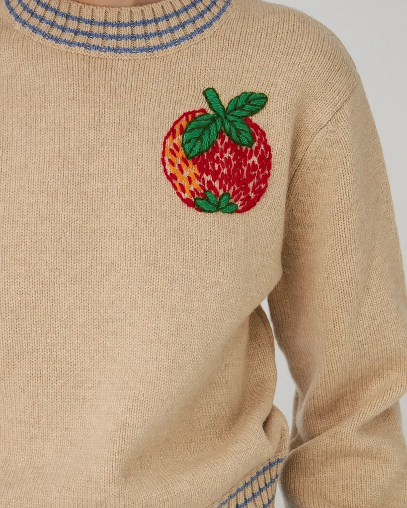 Krótki, beżowy sweter STELLA NOVA z dużym, haftowanym jabłkiem nad lewą piersią. Sweter ma okrągły dekolt i opadające ramiona. Wykończony jest ściągaczami i niebieskimi paskami przy dekolcie, mankietach i u dołu.