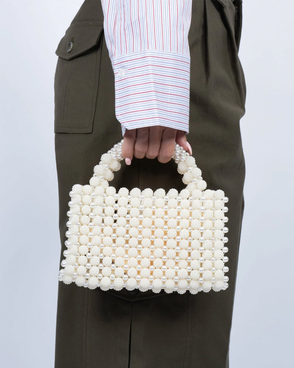 Ręcznie zdobiona torebka z pereł Pearl White SUI AVA. Jej kompaktowy rozmiar sprawia, że idealnie nadaje się na imprezy, kolacje lub jako elegancki dodatek do codziennych stylizacji. Dzięki solidnej konstrukcji perełek i eleganckiemu uchwytowi jest zarówno piękna, jak i funkcjonalna- idealna do noszenia najpotrzebniejszych rzeczy.