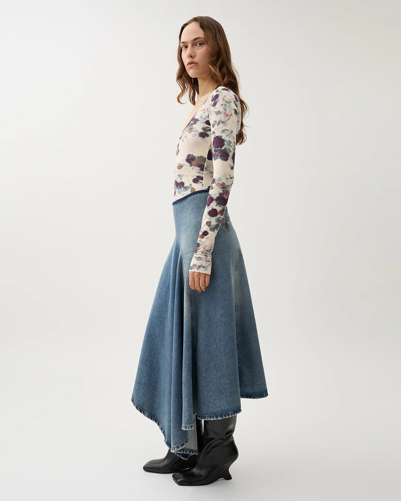 Długa, asymetryczna spódnica Swoosh Indigo z wysokim stanem, w niebieskim odcieniu denimu z przetarciami w stylu vintage i kwiatowymi haftami. U góry ma granatową lamówkę i zapięcie na suwak z boku.&nbsp;