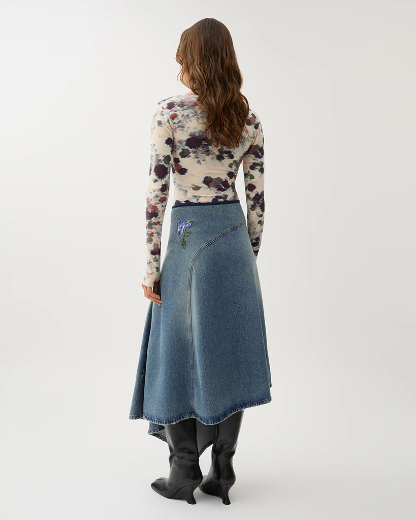 Długa, asymetryczna spódnica Swoosh Indigo z wysokim stanem, w niebieskim odcieniu denimu z przetarciami w stylu vintage i kwiatowymi haftami. U góry ma granatową lamówkę i zapięcie na suwak z boku.&nbsp;