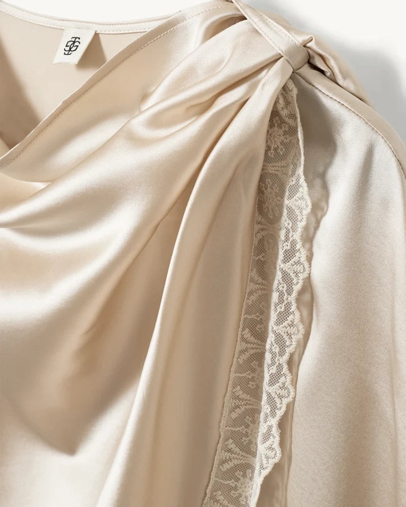 Elegancka, jedwabna peleryna Cata The Garment o asymetrycznym fasonie. Zebrana na lewym ramieniu. Wykończona zmysłową koronką. Wykonana z lejącej, jedwabnej tkaniny. 