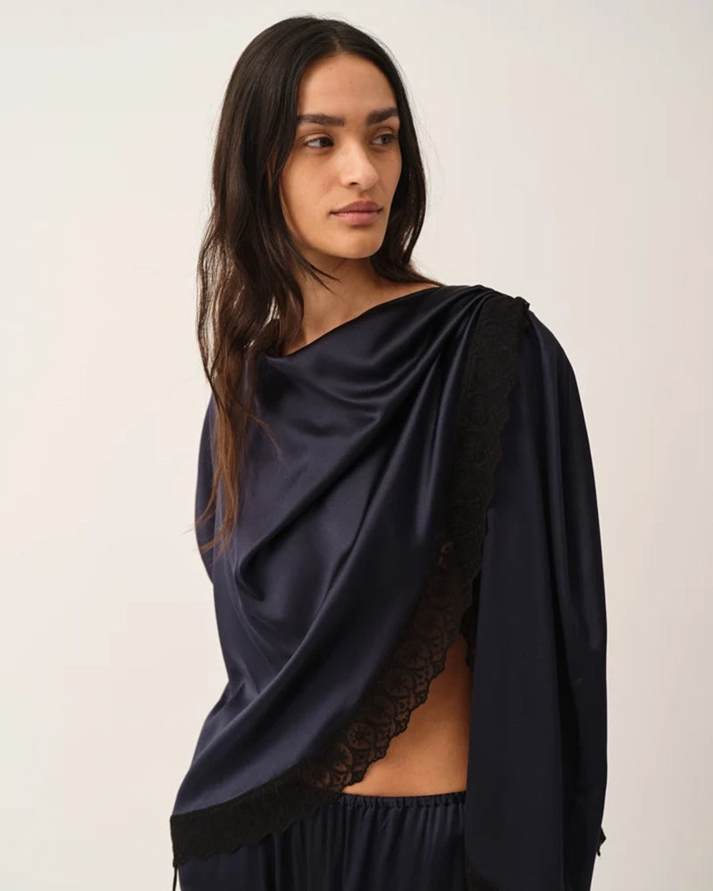 Elegancka, jedwabna peleryna Cata The Garment o asymetrycznym fasonie. Zebrana na lewym ramieniu. Wykończona zmysłową koronką. Wykonana z lejącej, jedwabnej tkaniny.