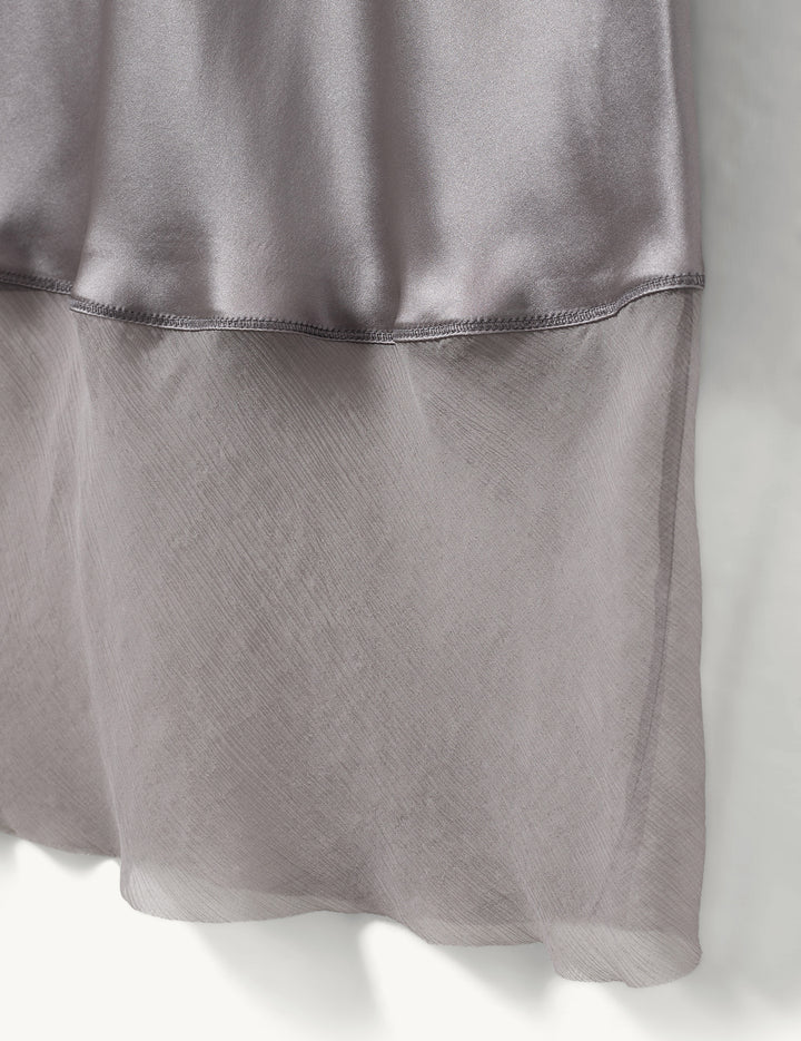 Luźna, jedwabna spódnica midi Catania The Garment z wysokim stanem. Elastyczna w talii. U dołu wykończona kontrastową, lekko transparentną, czarną tkaniną.