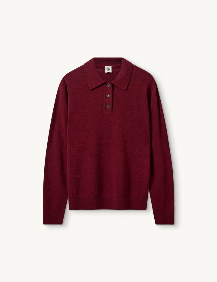 Luźny, długi, czerwony sweter Como Polo z kołnierzykiem i guzikami przy dekolcie. Sweter ma długie, luźne rękawy i wykończony jest ściągaczami. Posiada prosty krój i długość za biodra oraz niewielkie, haftowane logo.