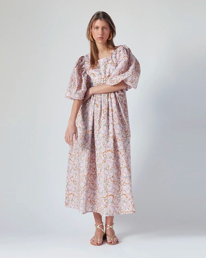 Luźna sukienka maxi Peggy The Label Edition w kwiatowy print z krótkimi, bufiastymi rękawami. Posiada kwadratowy dekolt oraz dwie, boczne kieszenie. Jest odcięta pod biustem. 