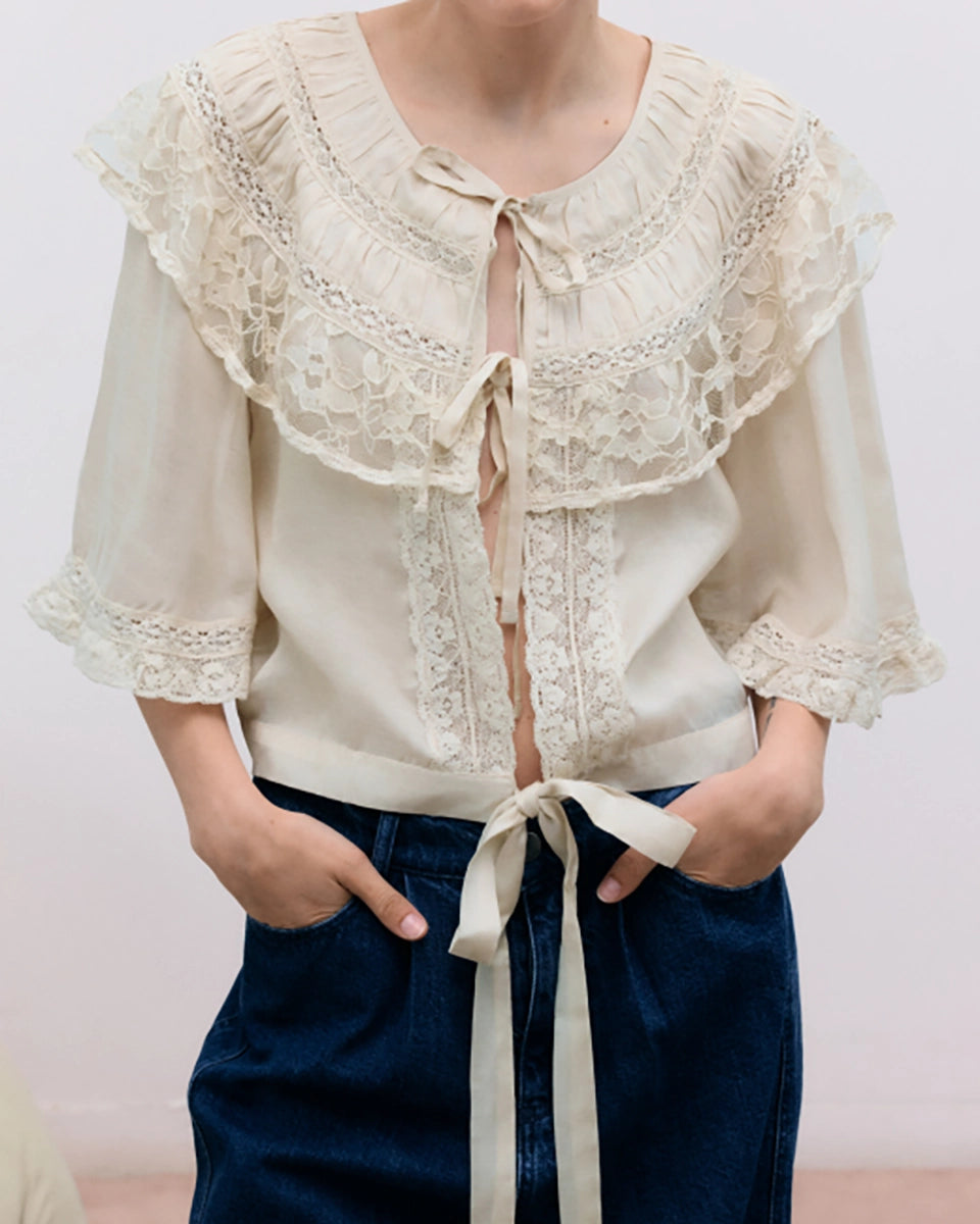 Romantyczna bluzka Ammi The New Society w stylu vintage z okrągłym dekoltem i szerokim rękawem za łokieć. Posiada efektowny, wykończony piękną koronką kołnierz. Z przodu wiązana na kokardki. Wykonana z tkaniny z jedwabiem