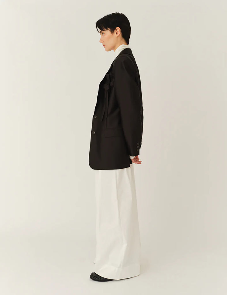 Klasyczna, jednorzędowa marynarka Umami Black o prostym kroju i długości za biodra. Zapinana na dwa guziki. Marynarka ma klapy i trójkątny dekolt. Posiada dwie, przednie kieszenie z klapkami. Wyróżnia się pięknym detalem przypominającym kokardę na kieszeni na piersi.&nbsp;